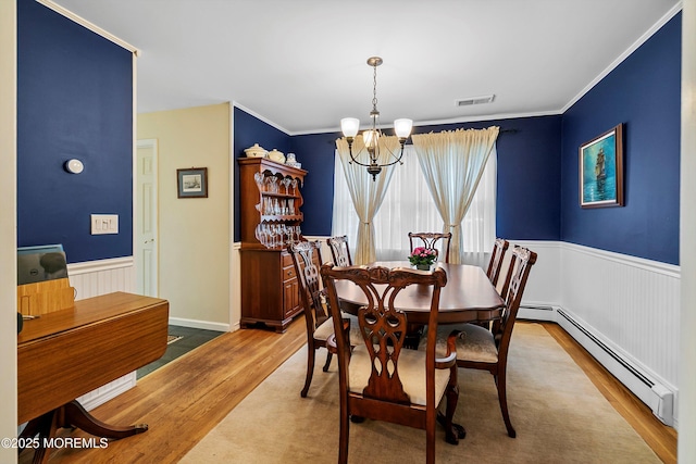 dining space with a chandelier, wood finished floors, a baseboard heating unit, a wainscoted wall, and crown molding