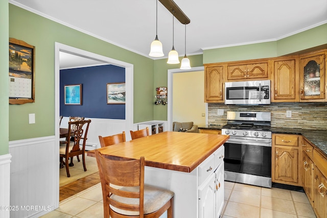 kitchen with stainless steel appliances, light tile patterned flooring, tasteful backsplash, a wainscoted wall, and hanging light fixtures