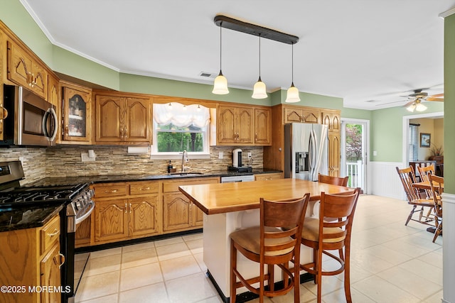 kitchen with stainless steel appliances, a sink, brown cabinetry, plenty of natural light, and a wainscoted wall