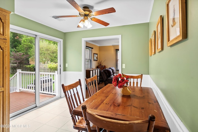 dining area with ceiling fan, crown molding, a wainscoted wall, and light tile patterned floors