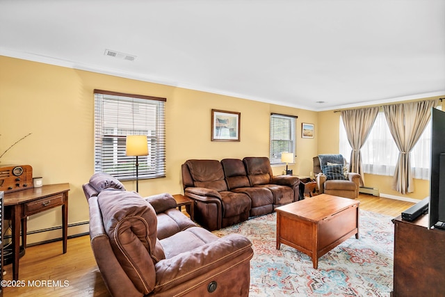 living area featuring ornamental molding, light wood-style floors, baseboard heating, and healthy amount of natural light
