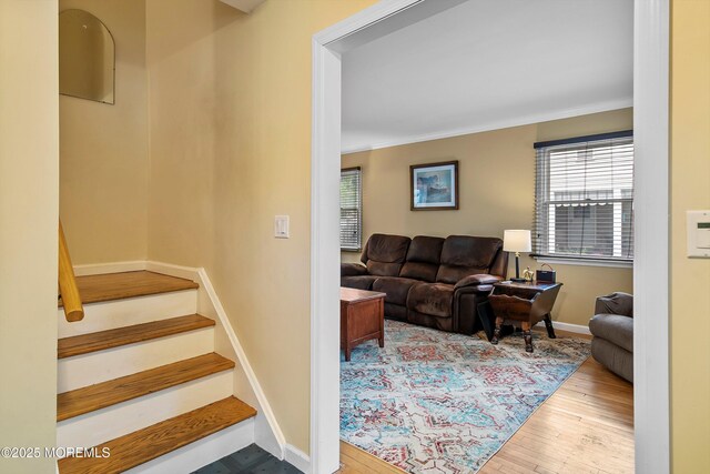 living area with wood finished floors, ornamental molding, stairs, and baseboards