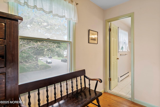corridor featuring a baseboard radiator, wood finished floors, plenty of natural light, and baseboards