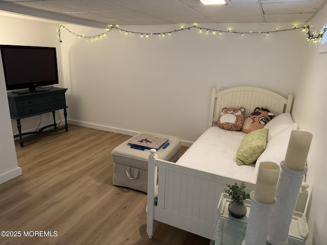 bedroom featuring wood finished floors, a drop ceiling, and baseboards