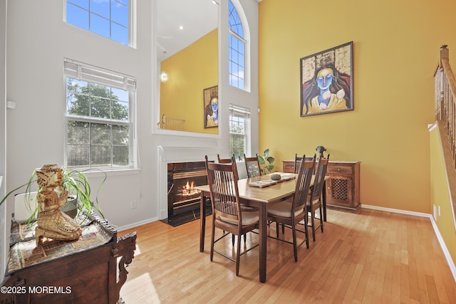 dining space with a towering ceiling, healthy amount of natural light, baseboards, and a fireplace with flush hearth