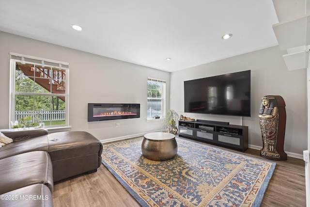 living area with a glass covered fireplace, wood finished floors, baseboards, and recessed lighting