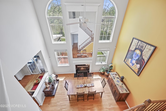 living area with a towering ceiling, ceiling fan, wood finished floors, and healthy amount of natural light