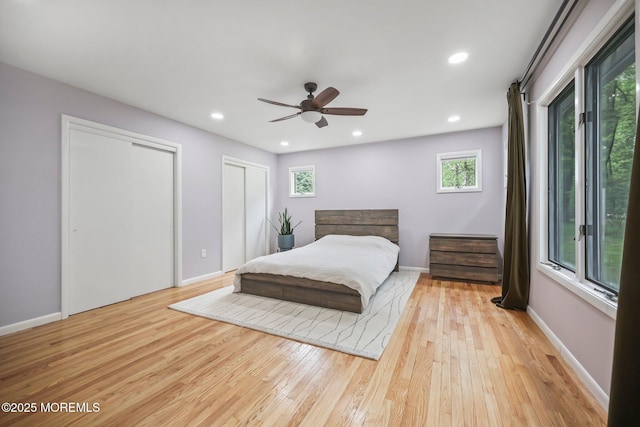 bedroom with two closets, light wood-style flooring, baseboards, recessed lighting, and a ceiling fan
