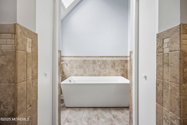 bathroom featuring tile walls, a freestanding tub, a wainscoted wall, and a skylight
