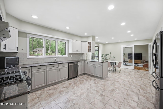 kitchen with appliances with stainless steel finishes, a sink, tasteful backsplash, recessed lighting, and dark stone countertops