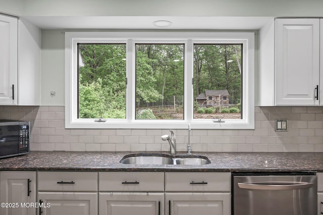 kitchen with stainless steel dishwasher, a sink, white cabinetry, dark stone counters, and backsplash