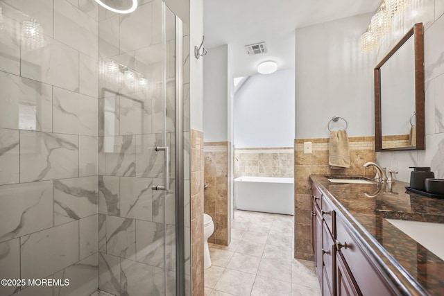 full bath featuring double vanity, a stall shower, a freestanding bath, tile walls, and toilet