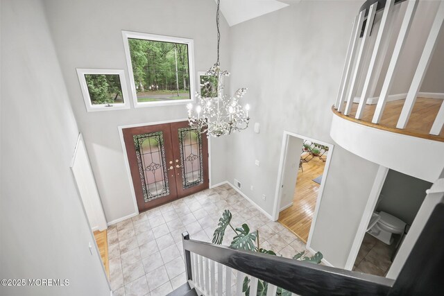 tiled entrance foyer featuring high vaulted ceiling, french doors, a chandelier, and baseboards