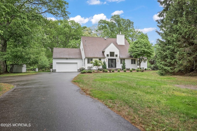 view of front of home with asphalt driveway, a garage, a chimney, a front yard, and a shingled roof