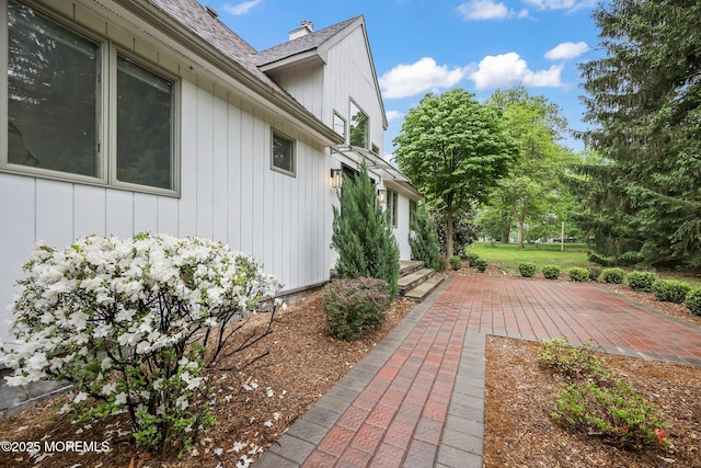 view of side of home with roof with shingles, a patio area, and a chimney
