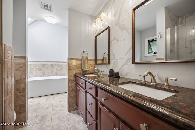 full bath featuring tile walls, a freestanding bath, double vanity, and tile patterned flooring