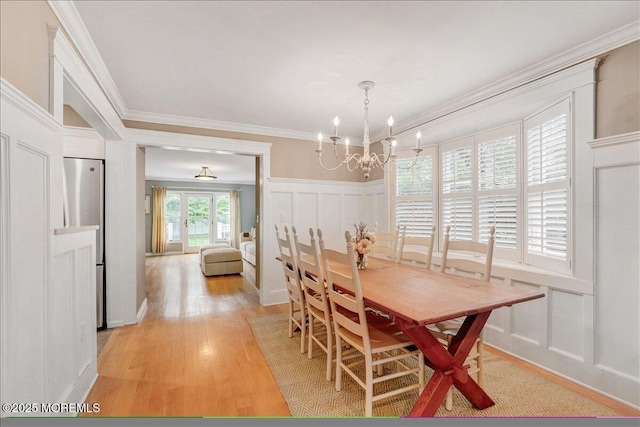 dining space with a decorative wall, a chandelier, ornamental molding, light wood finished floors, and a wainscoted wall