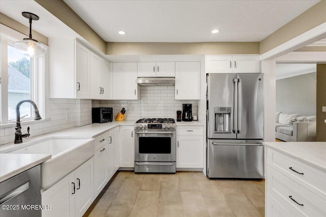 kitchen with appliances with stainless steel finishes, under cabinet range hood, backsplash, light countertops, and white cabinetry