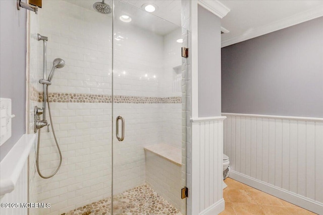 full bath featuring a stall shower, toilet, a wainscoted wall, ornamental molding, and tile patterned flooring