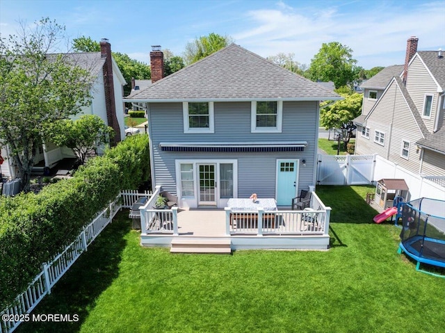 rear view of property featuring a trampoline, a wooden deck, a shingled roof, a gate, and a chimney