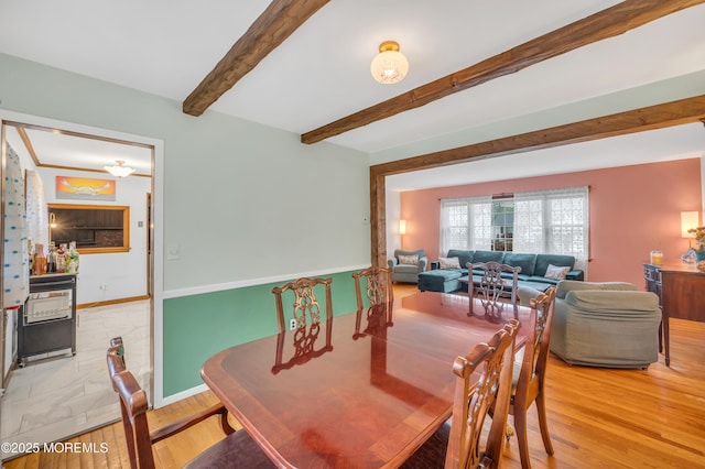 dining space with light wood finished floors, beam ceiling, and baseboards