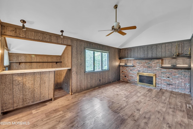 unfurnished living room with a ceiling fan, vaulted ceiling, wood finished floors, wood walls, and a fireplace