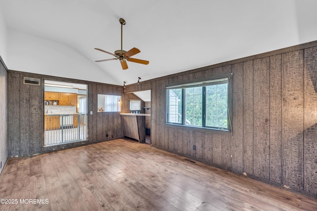 spare room with wood walls, ceiling fan, lofted ceiling, and hardwood / wood-style flooring