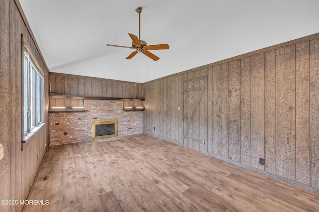 unfurnished living room featuring a ceiling fan, wood finished floors, wood walls, a fireplace, and high vaulted ceiling