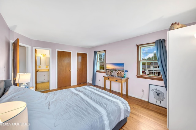 bedroom featuring multiple windows, light wood-type flooring, two closets, and baseboards