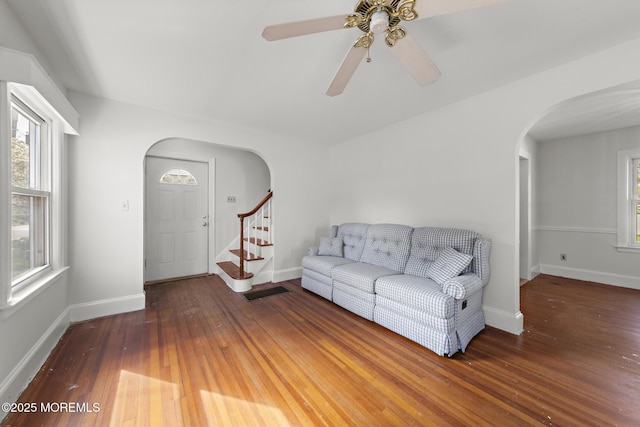 living room with arched walkways, hardwood / wood-style floors, a ceiling fan, stairway, and baseboards