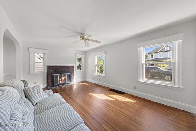 living room featuring wood finished floors, baseboards, a ceiling fan, a fireplace, and arched walkways