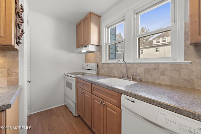 kitchen featuring white appliances, a sink, under cabinet range hood, light wood finished floors, and backsplash