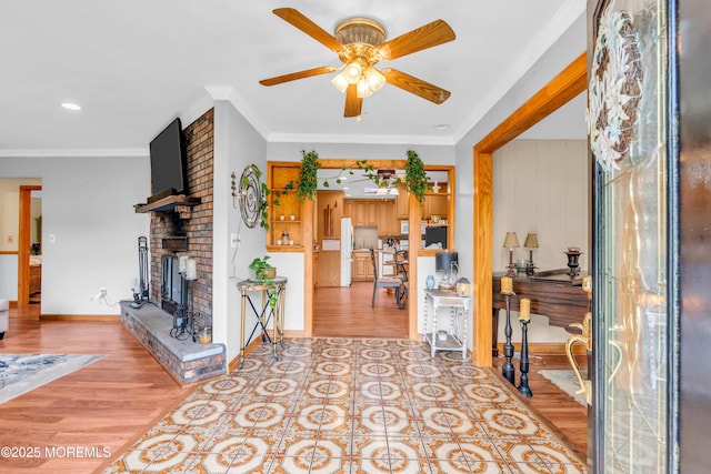 living area featuring a ceiling fan, a fireplace, light wood-style floors, ornamental molding, and baseboards
