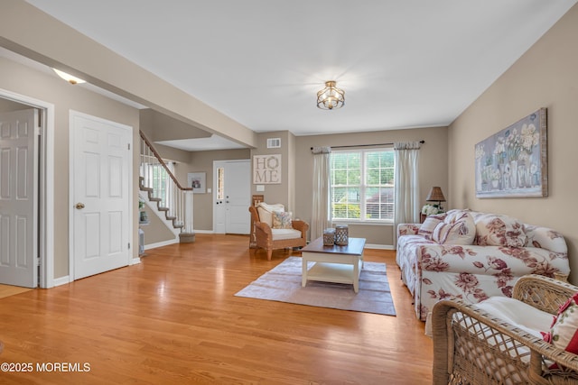 living area featuring light wood finished floors, stairway, and baseboards