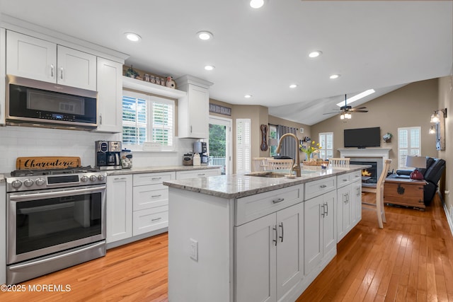 kitchen with appliances with stainless steel finishes, a sink, a warm lit fireplace, ceiling fan, and open floor plan