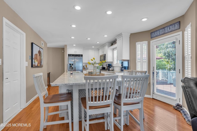 kitchen with stainless steel appliances, white cabinets, light wood-style flooring, light stone countertops, and a kitchen breakfast bar