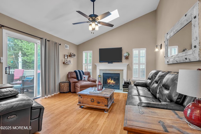 living area with light wood-type flooring, ceiling fan, a fireplace, high vaulted ceiling, and a skylight