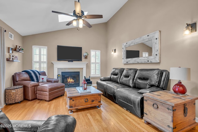 living area featuring vaulted ceiling, a ceiling fan, wood finished floors, and a fireplace with flush hearth
