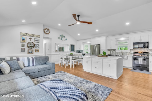 living room featuring ceiling fan, vaulted ceiling, light wood-style flooring, a wainscoted wall, and recessed lighting