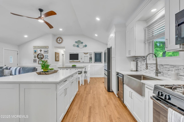 kitchen featuring appliances with stainless steel finishes, lofted ceiling, white cabinets, a center island, and ceiling fan
