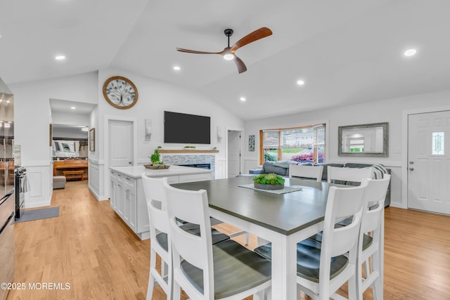 dining area featuring vaulted ceiling, light wood-style floors, a fireplace, and a ceiling fan