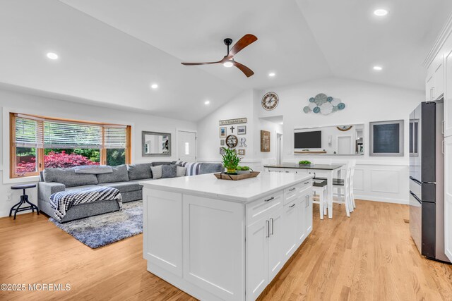 kitchen with freestanding refrigerator, lofted ceiling, white cabinetry, a ceiling fan, and a center island