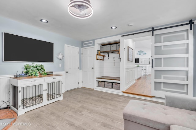 living area with a barn door, a wainscoted wall, light wood-style flooring, and recessed lighting