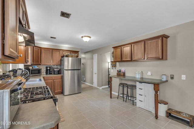 2465 Woodland Rd, Manchester, NJ 08759 - kitchen featuring appliances with stainless steel finishes, under cabinet range hood, brown cabinetry, baseboards, and a breakfast bar area