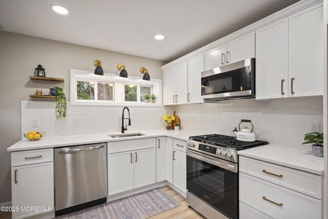 kitchen featuring stainless steel appliances, a sink, white cabinets, backsplash, and light wood-style flooring