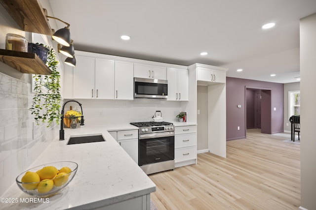 kitchen featuring stainless steel appliances, a sink, backsplash, white cabinetry, and recessed lighting