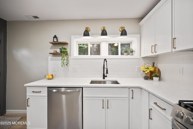 kitchen with appliances with stainless steel finishes, a sink, backsplash, white cabinetry, and light countertops