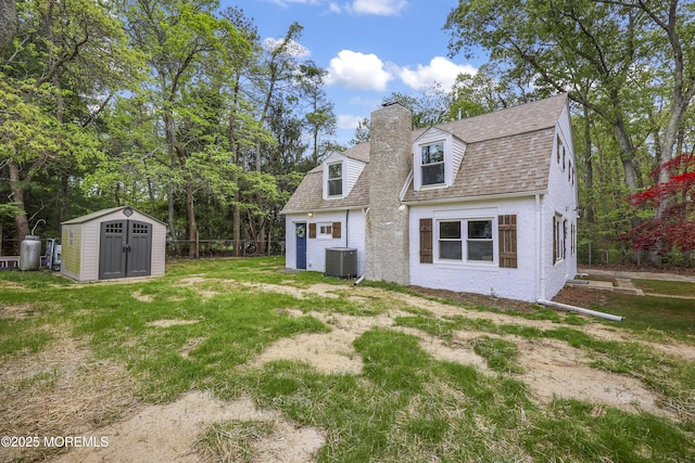 rear view of property with central AC, a storage shed, a chimney, an outbuilding, and a shingled roof