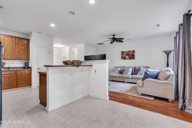 kitchen featuring a ceiling fan, brown cabinetry, open floor plan, recessed lighting, and light flooring