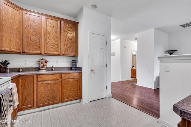 kitchen featuring brown cabinetry, baseboards, stove, and light floors